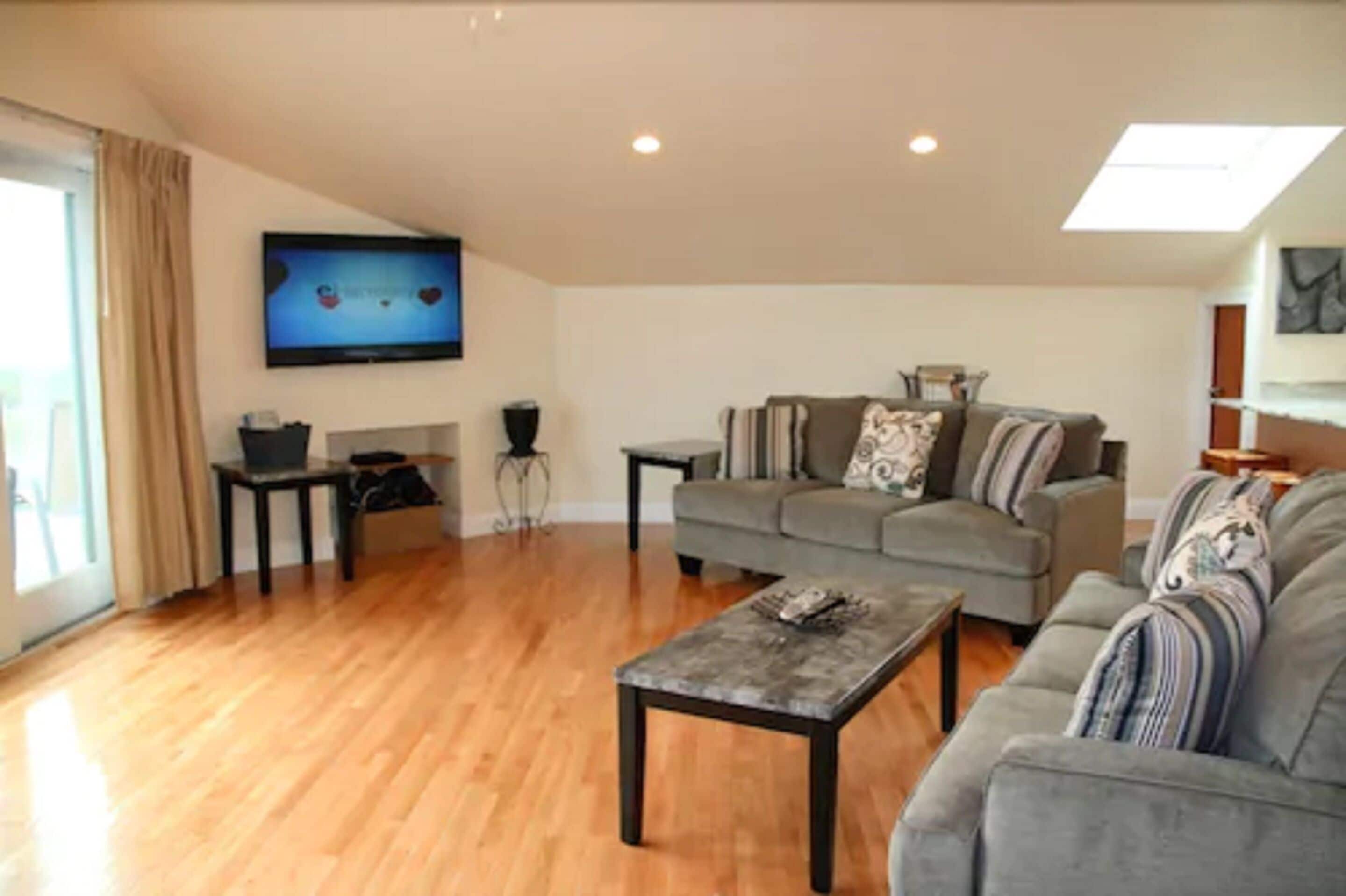 A living room with a grey sofa, a coffee table, and a flat-screen TV mounted on the wall.