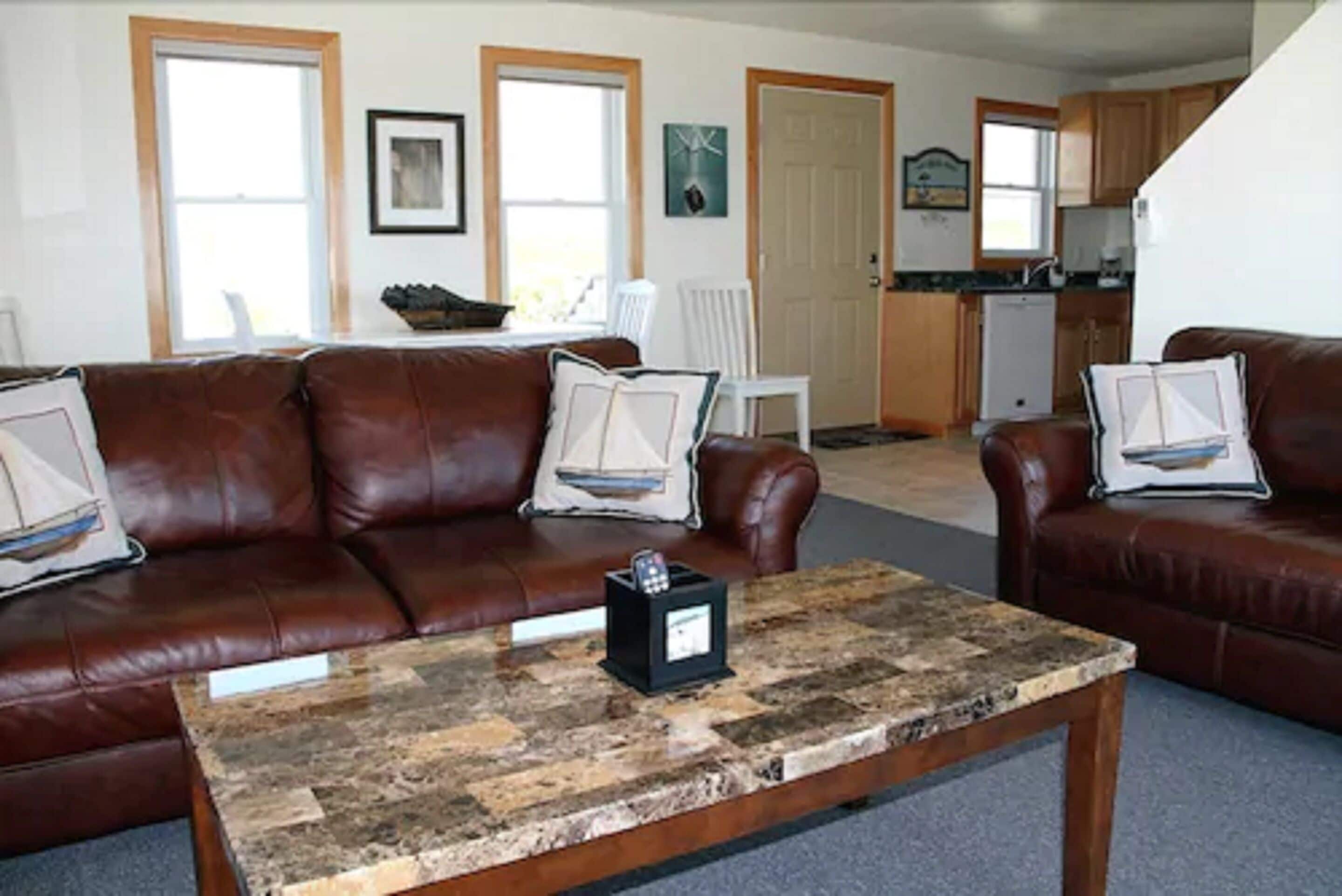 A living room with a brown leather sofa, a coffee table, and a kitchen in the background.