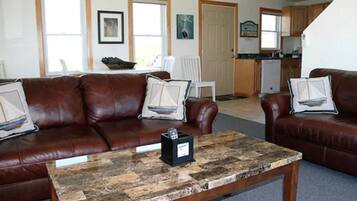 A living room with a brown leather sofa, a coffee table, and a kitchen in the background.