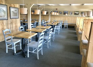 A restaurant with wooden tables and chairs, hanging pendant lights, and framed pictures on the walls. - Top Mast Resort (North Truro)