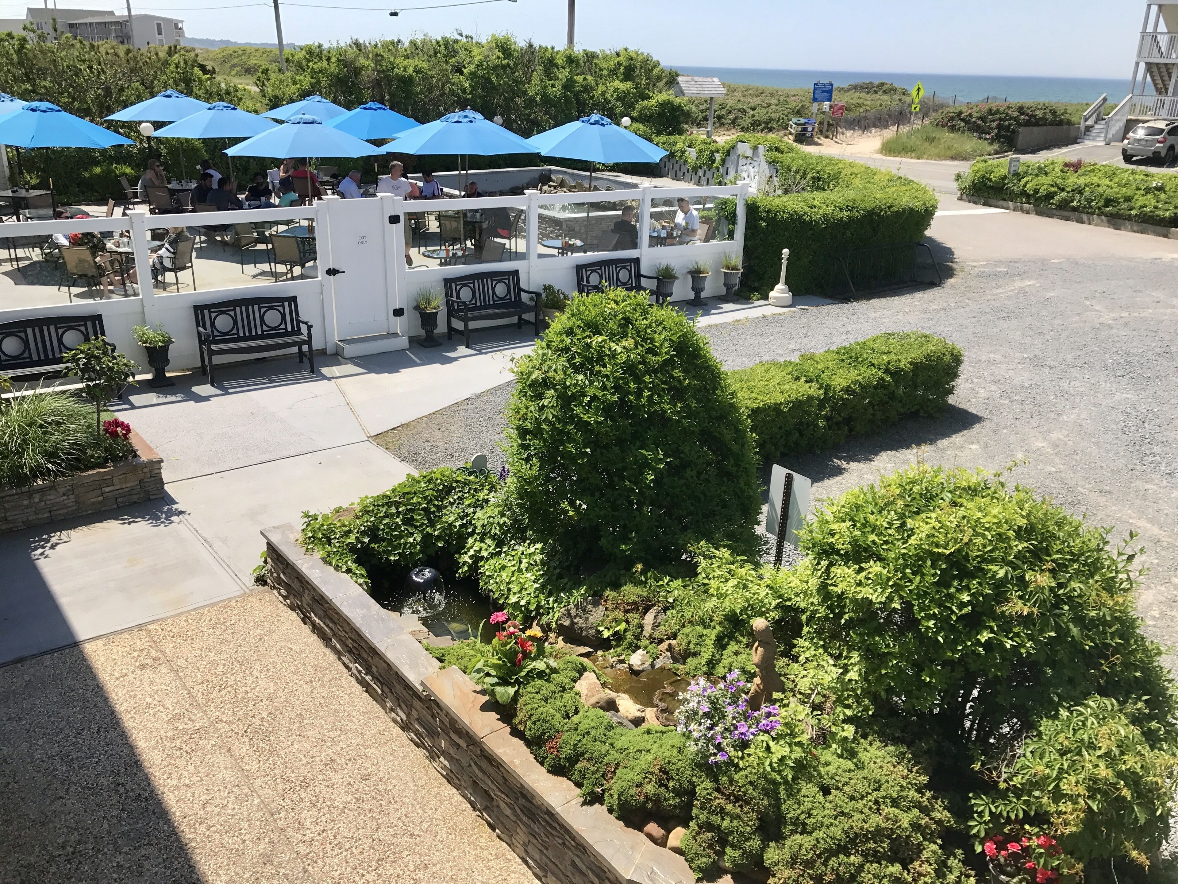 Un restaurant en plein air avec des parasols bleus, des tables et une vue sur l’océan.