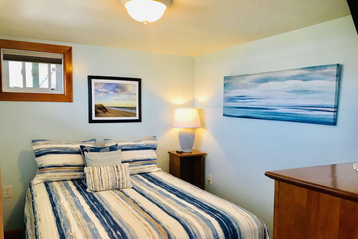 A bedroom with a bed, a nightstand, a lamp, and two framed pictures on the wall.