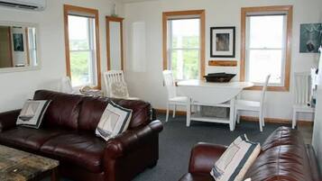 A living room with a brown leather sofa, a coffee table, and a dining table with chairs.