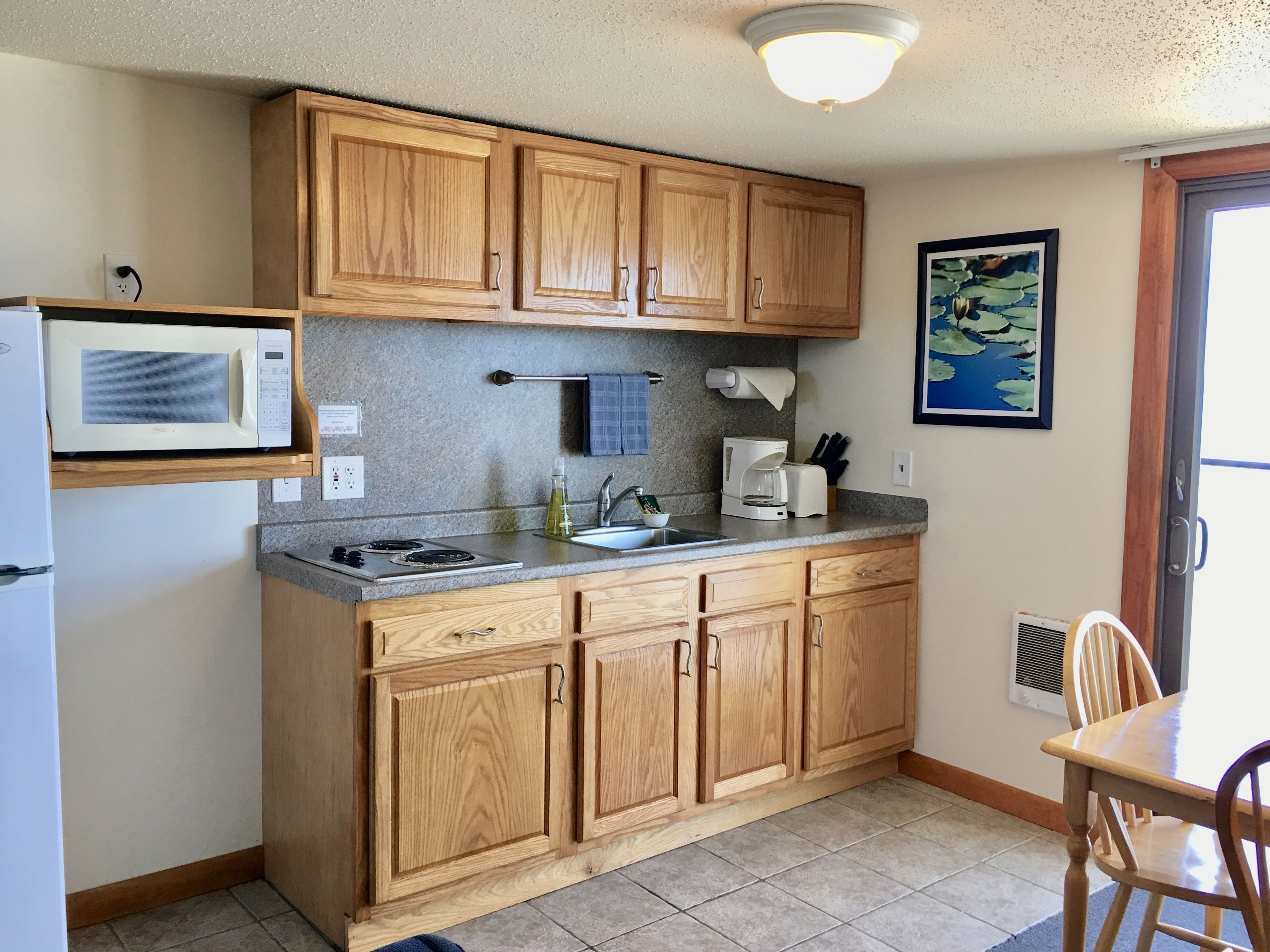 A compact kitchen with wooden cabinets, a microwave, a sink, and a coffee maker.