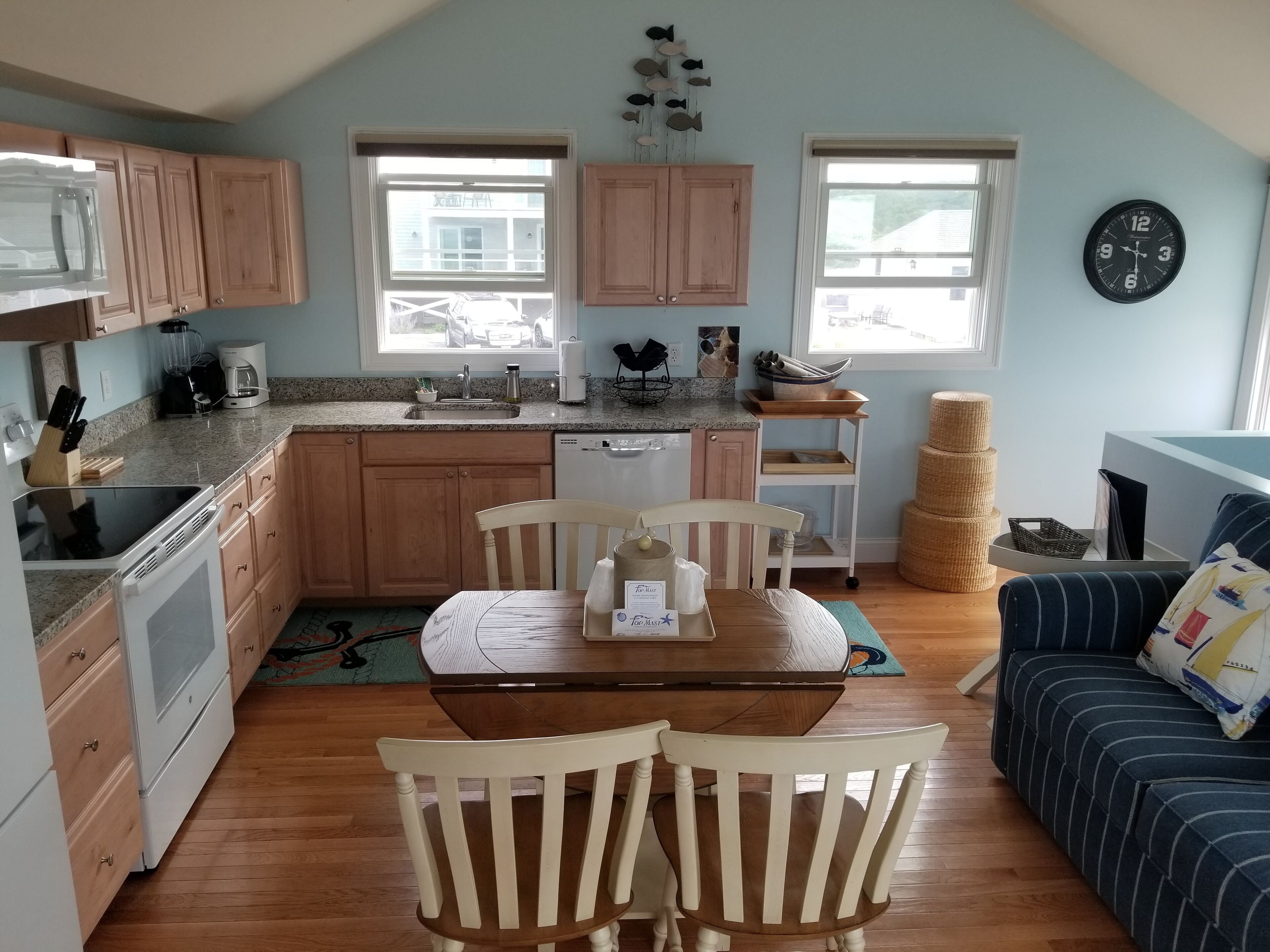 A kitchen with wooden cabinets, a dining table with chairs, a clock, and a blue couch.
