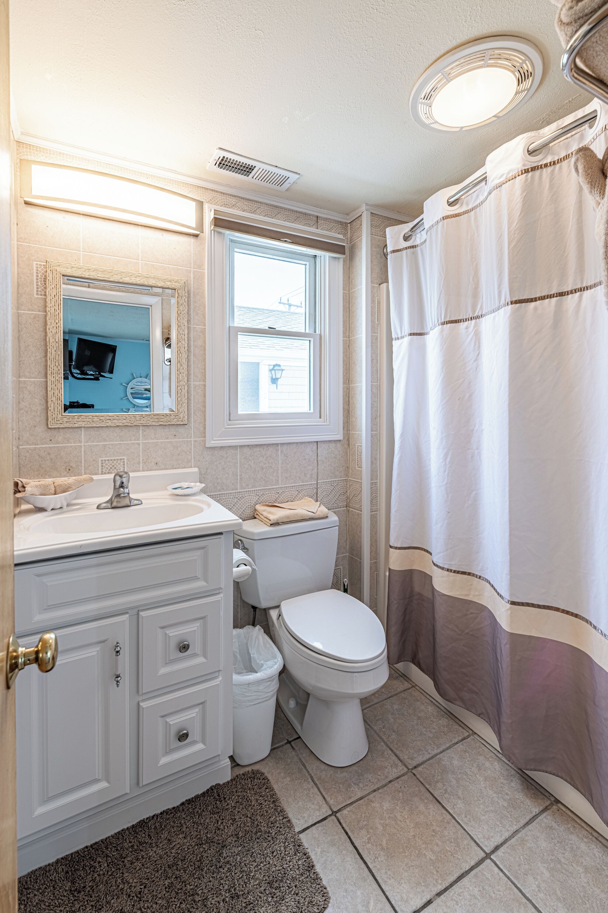 A bathroom with a white sink, mirror, and toilet, a window, and a shower curtain.