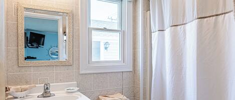A bathroom with a white sink, mirror, and toilet, a window, and a shower curtain.