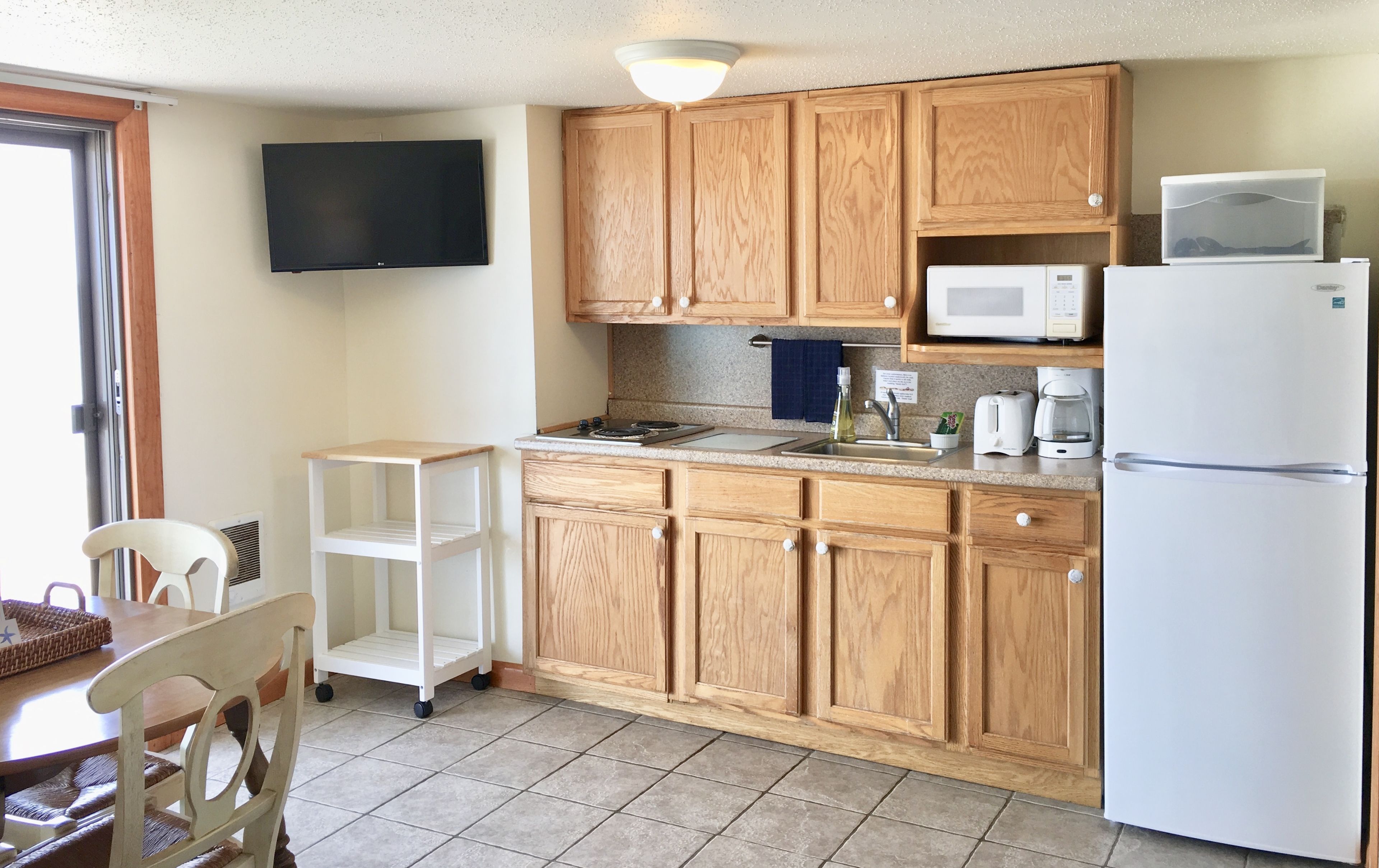 A kitchen with wooden cabinets, a microwave, a refrigerator, a sink, and a small table with chairs.