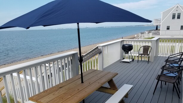 A wooden deck with a table and benches, overlooking a beach and ocean. - Top Mast Resort (North Truro)