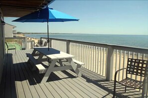 A wooden deck with a picnic table and chairs, overlooking a beach. - Top Mast Resort (North Truro)