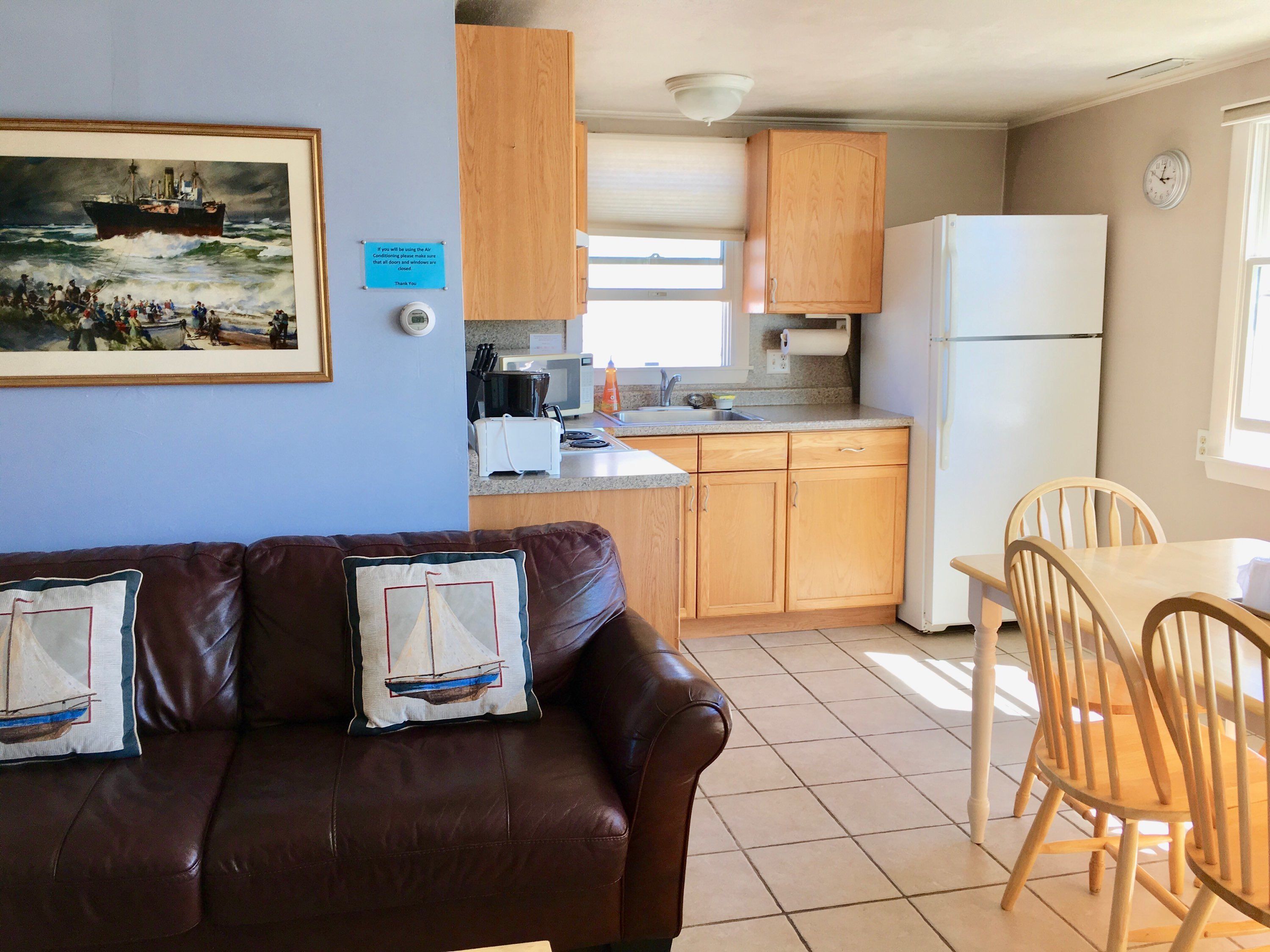 Una cocina compacta con armarios de madera, una mesa de comedor con sillas, un refrigerador y un cuadro en la pared.