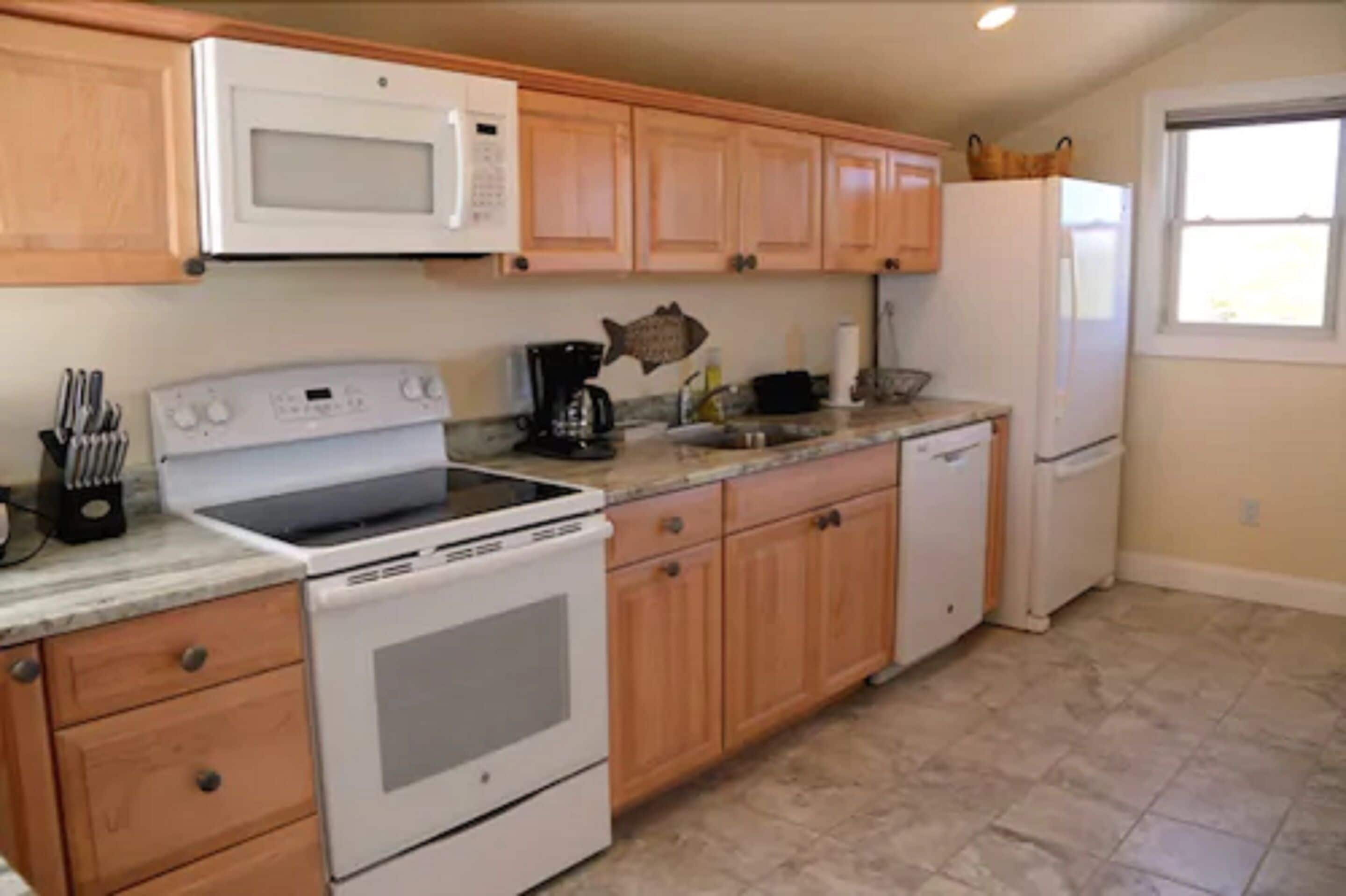 A kitchen with wooden cabinets, a microwave, a stove, a coffee maker, and a refrigerator.