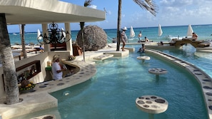 A pool area with a bar, lounge chairs, and a view of the ocean. - Nasim Condo Hotel acceso Gratis Beach Club, a metros 5th Avenida (Playa del Carmen)