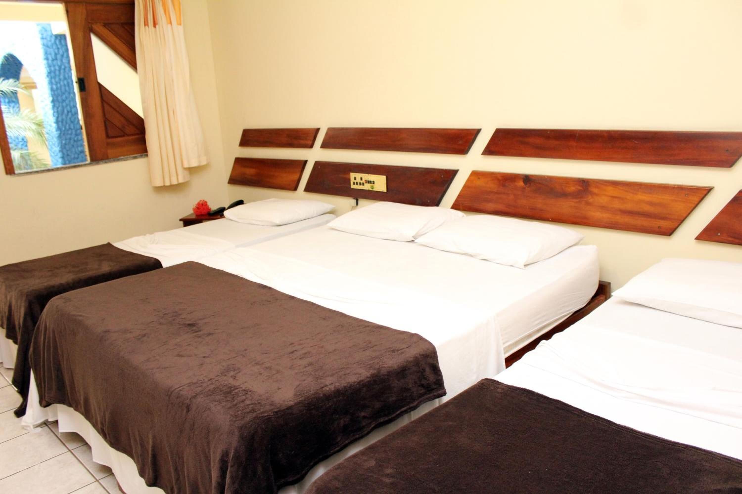 A hotel room with three beds, each with a brown bedspread and white pillows. The headboard is wooden with a plaque.