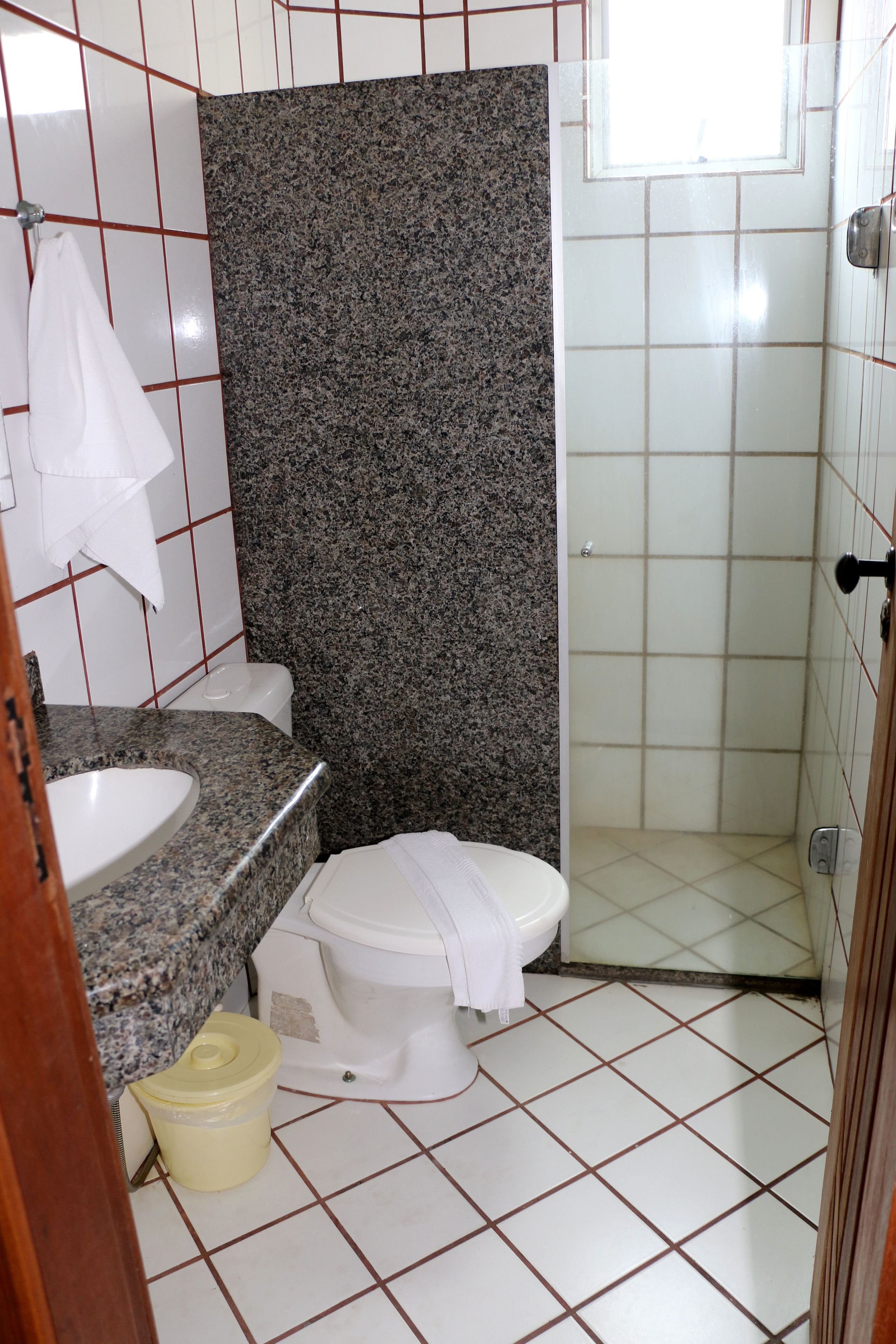 A bathroom with a granite countertop, white toilet, and a shower area.