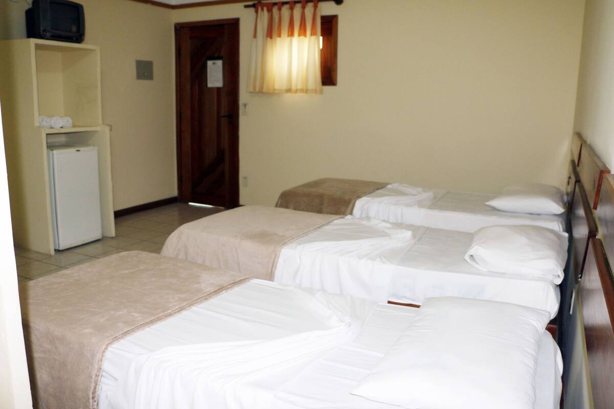 Une chambre d’hôtel avec trois lits simples, un petit réfrigérateur et une porte en bois.
