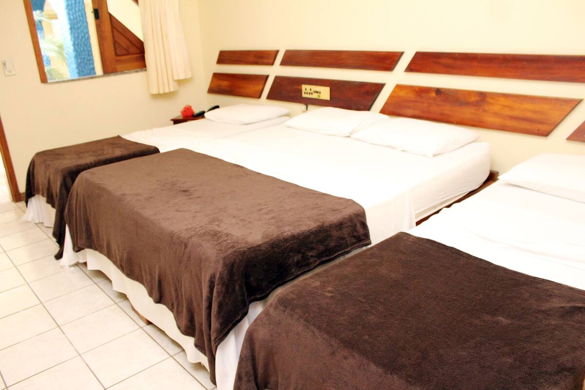 Une chambre d’hôtel avec trois lits simples, chacun recouvert d’une couverture marron et agrémenté d’oreillers blancs.