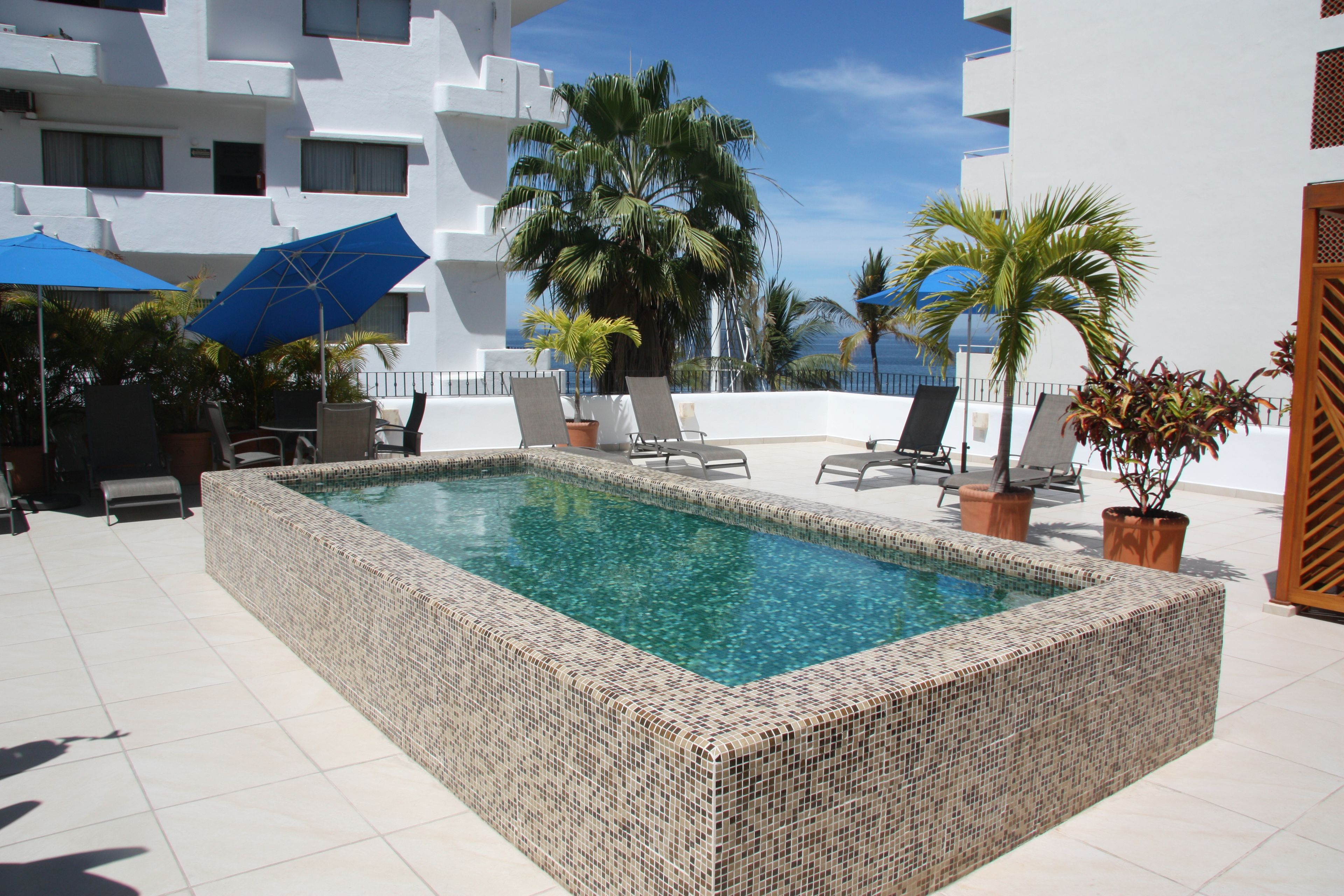 A rectangular pool with mosaic tiles, surrounded by lounge chairs and potted plants.