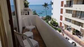 Een balkon met witte plastic stoelen, uitzicht op zee met boten, en een gebouw met balkons en een bordje voor een salon.