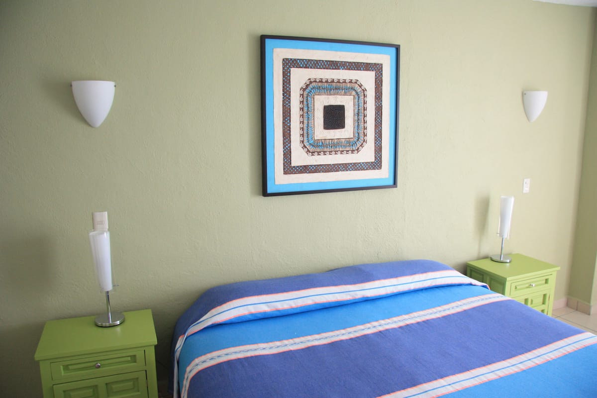 Une chambre à coucher avec un lit, des tables de chevet vertes et une œuvre d’art encadrée accrochée au mur.