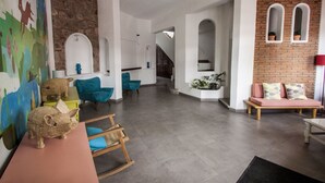Een ruime woonkamer met een groot wanddecoratie, een houten schommelstoel, een roze bank en een trap naar een ander niveau.