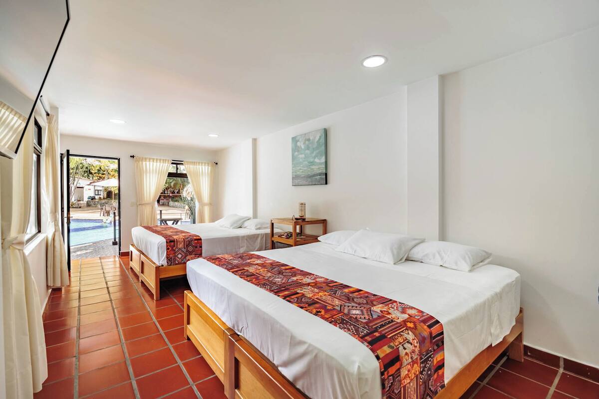 A hotel room with two beds, a small table, and a painting on the wall.