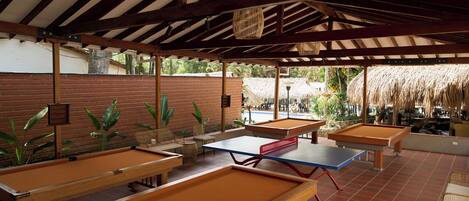 A covered outdoor area with multiple pool tables and chairs.