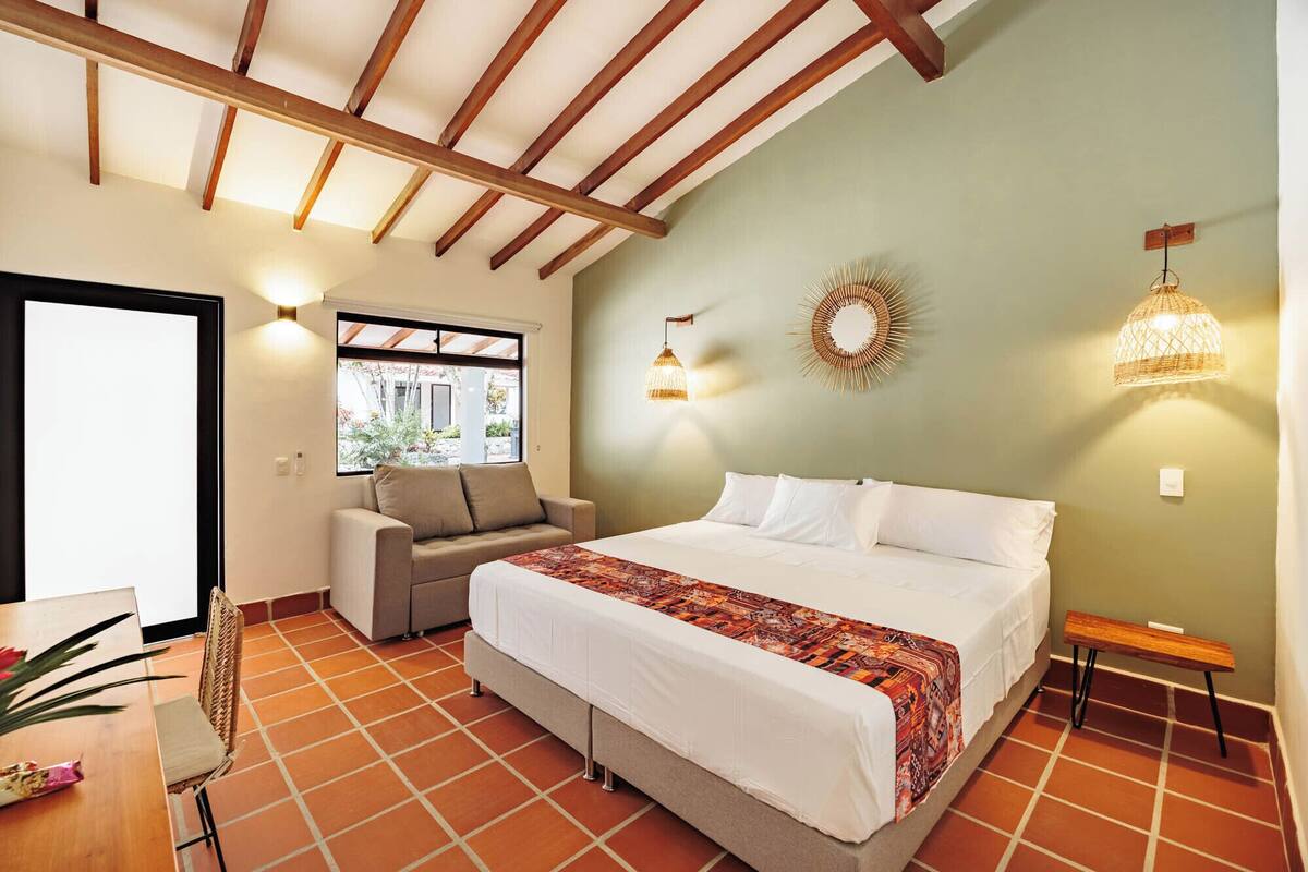 A bedroom with a bed, a sofa, a dining table, and a chair.