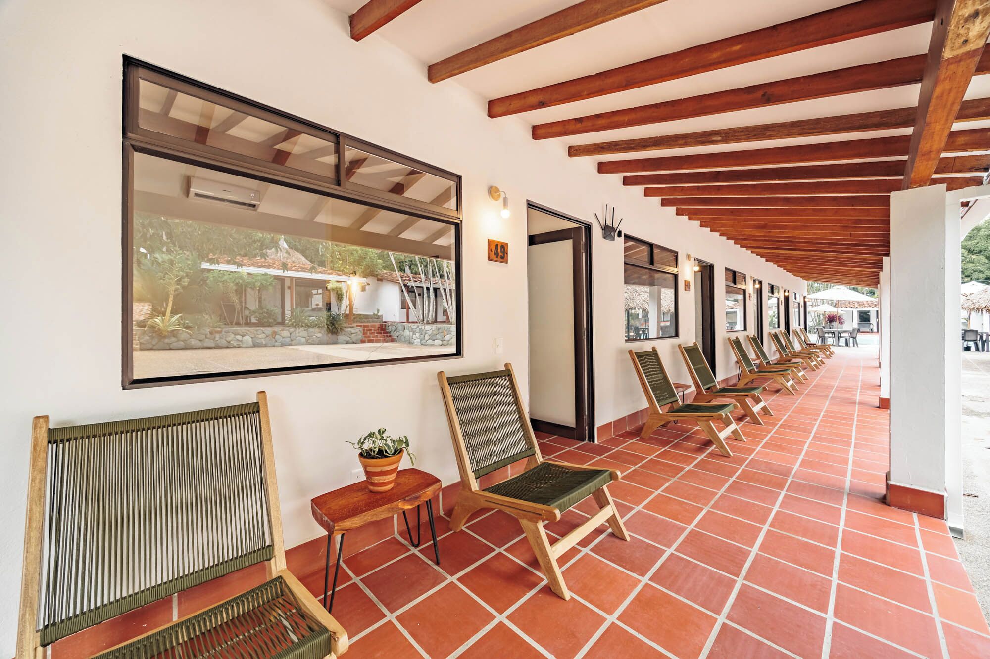 A covered outdoor seating area with wooden chairs and a large window overlooking a garden.
