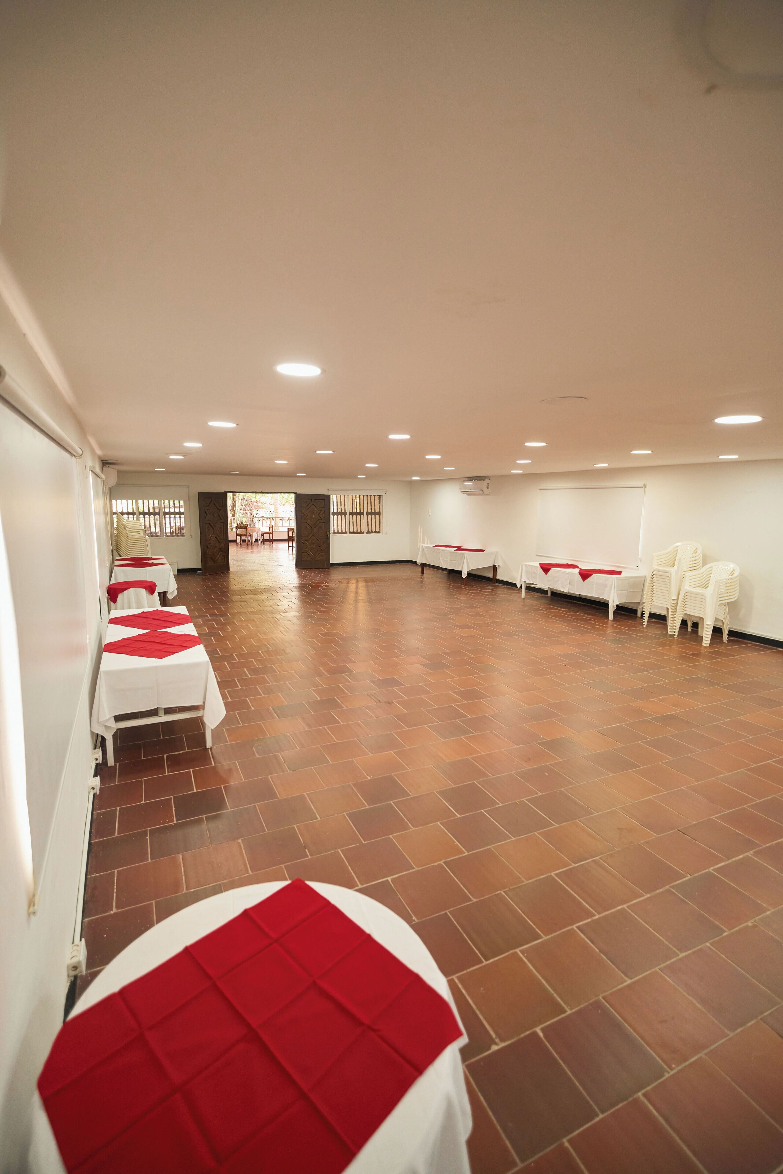 Un salón amplio con mesas blancas y manteles rojos, dispuestas en filas.