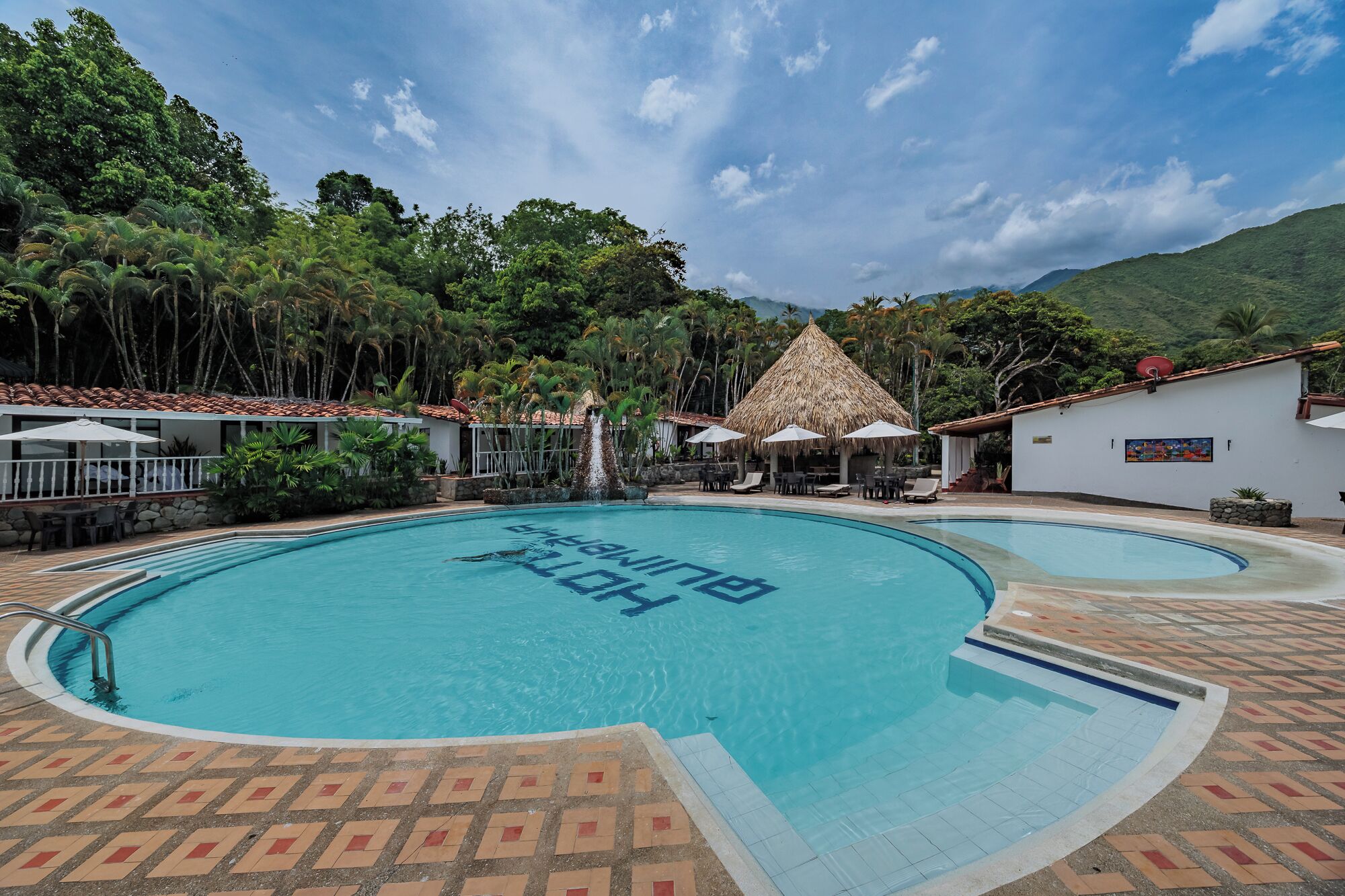 A swimming pool with a tropical setting, surrounded by lush greenery and a mountain in the background.