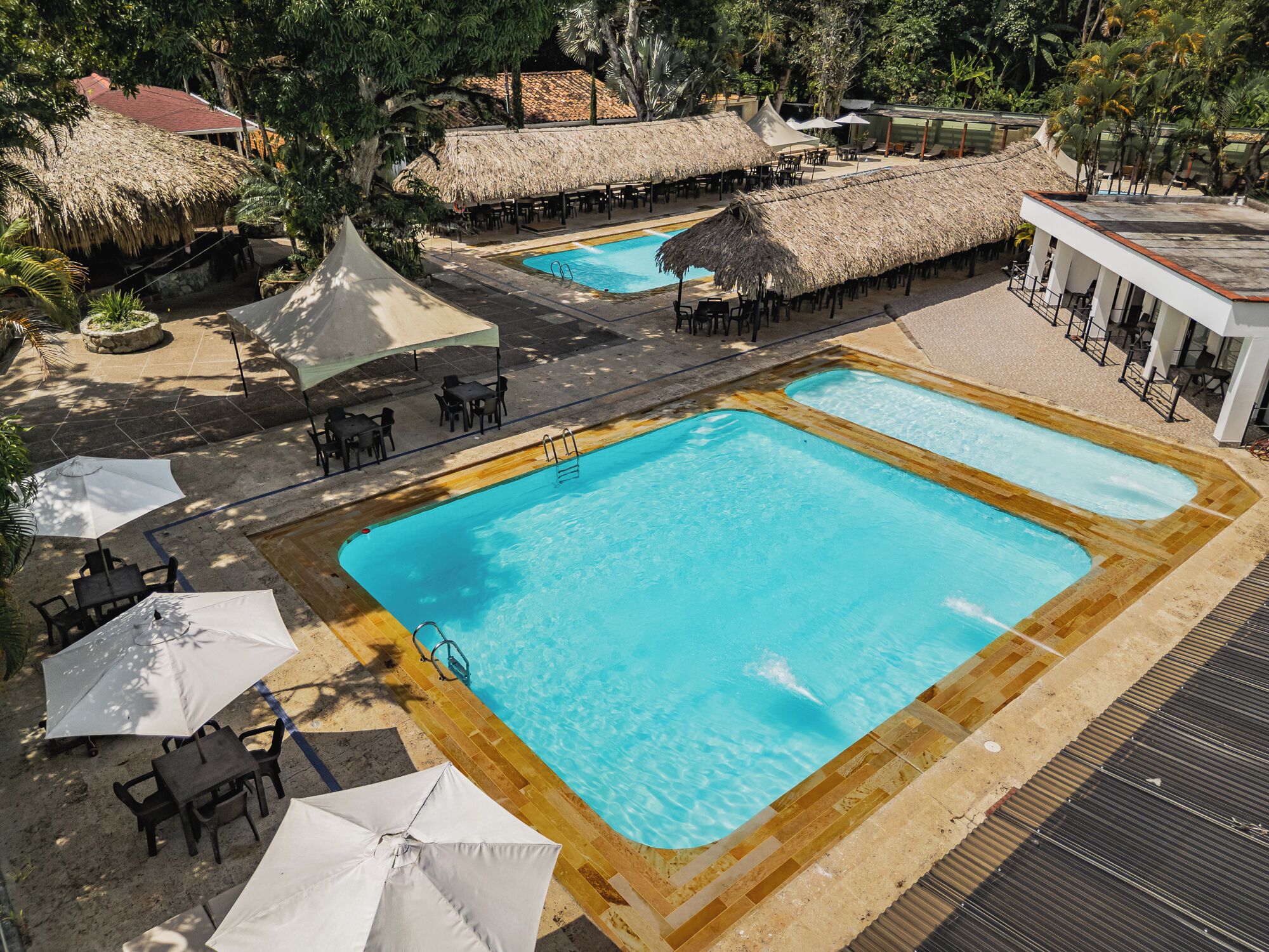 A pool area with two rectangular pools, surrounded by thatched-roof structures and outdoor seating.