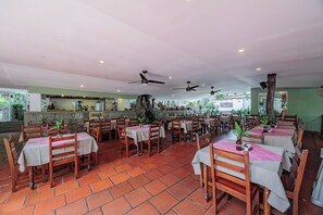 A restaurant with multiple tables and chairs, ceiling fans, and a stone wall in the background. - Hotel Quimbaya (San Jerónimo)