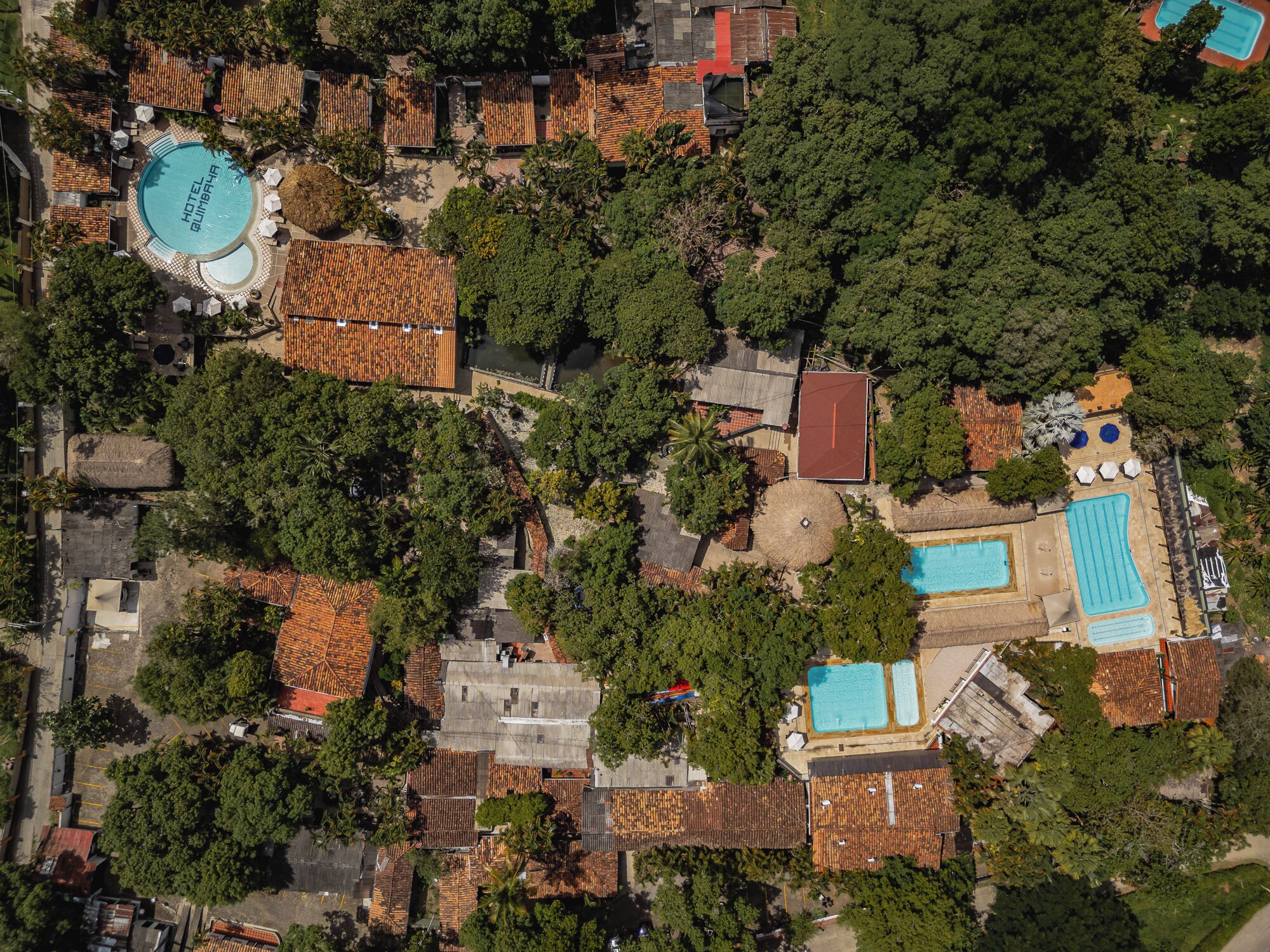Vista aérea de un complejo turístico con varias piscinas, una piscina central grande y diversas cabañas rodeadas de exuberante vegetación tropical.