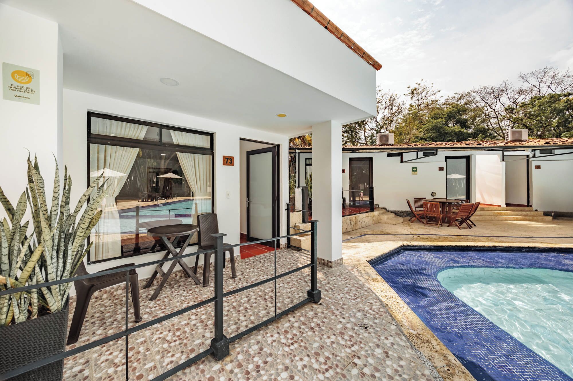 A modern outdoor pool area with a glass enclosure, a seating area with chairs, and a small pool.