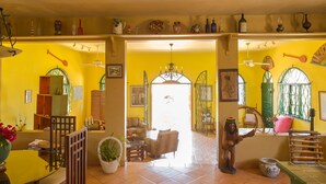A bright yellow interior with a dining area, a living room with a sofa and chairs, and a statue of a person holding a guitar. - Sundown Villa -Negril (Negril)