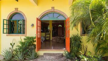 A yellow building with an open entrance, a tiled patio, and various plants.