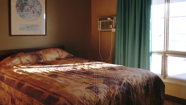 A bedroom with a large bed, a wall-mounted air conditioner, and a window with curtains. - The Ritz Cafe and Motor Inn (Whitecourt)