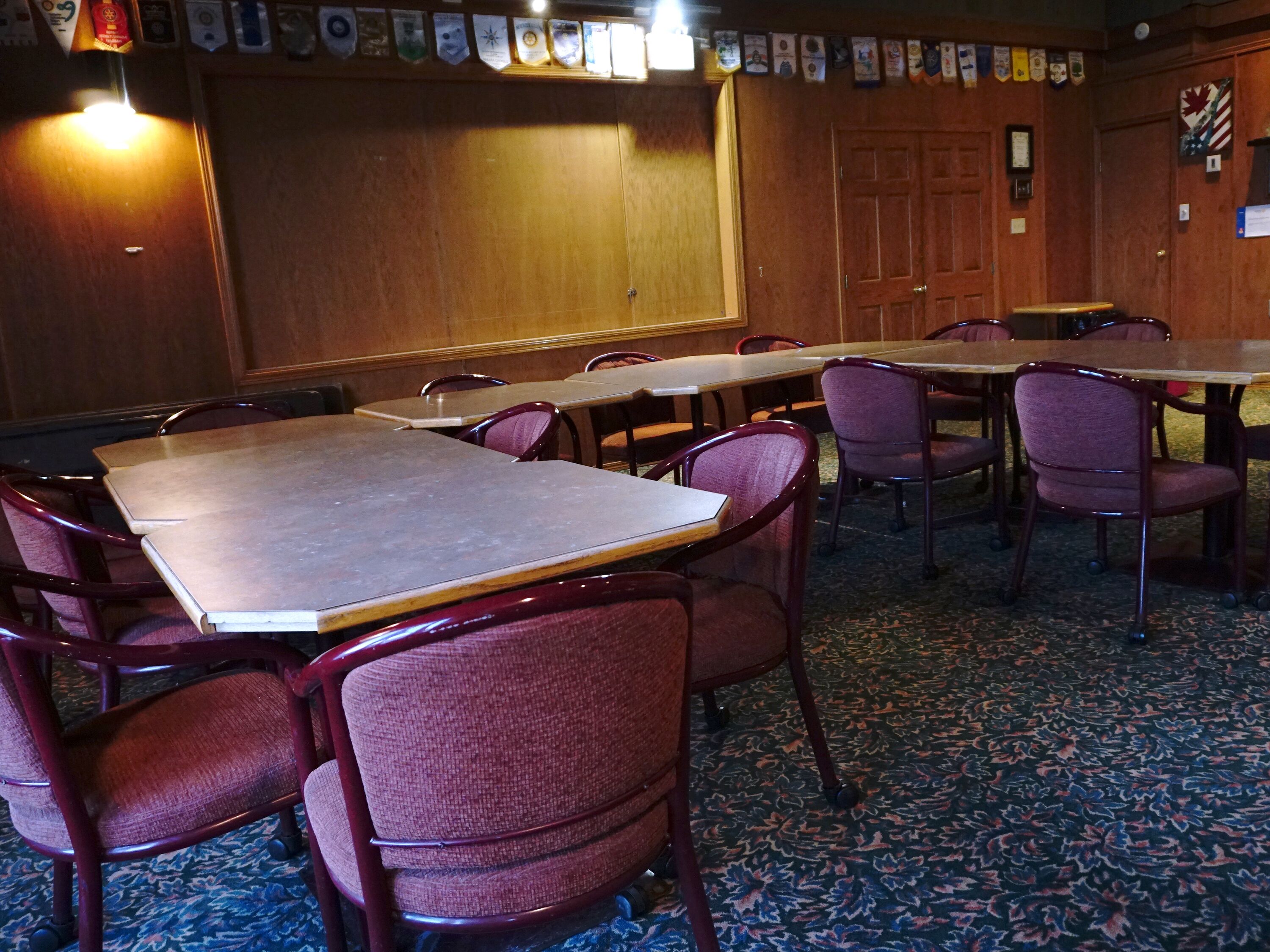 A conference room with tables and chairs, a wooden door, and a carpeted floor.