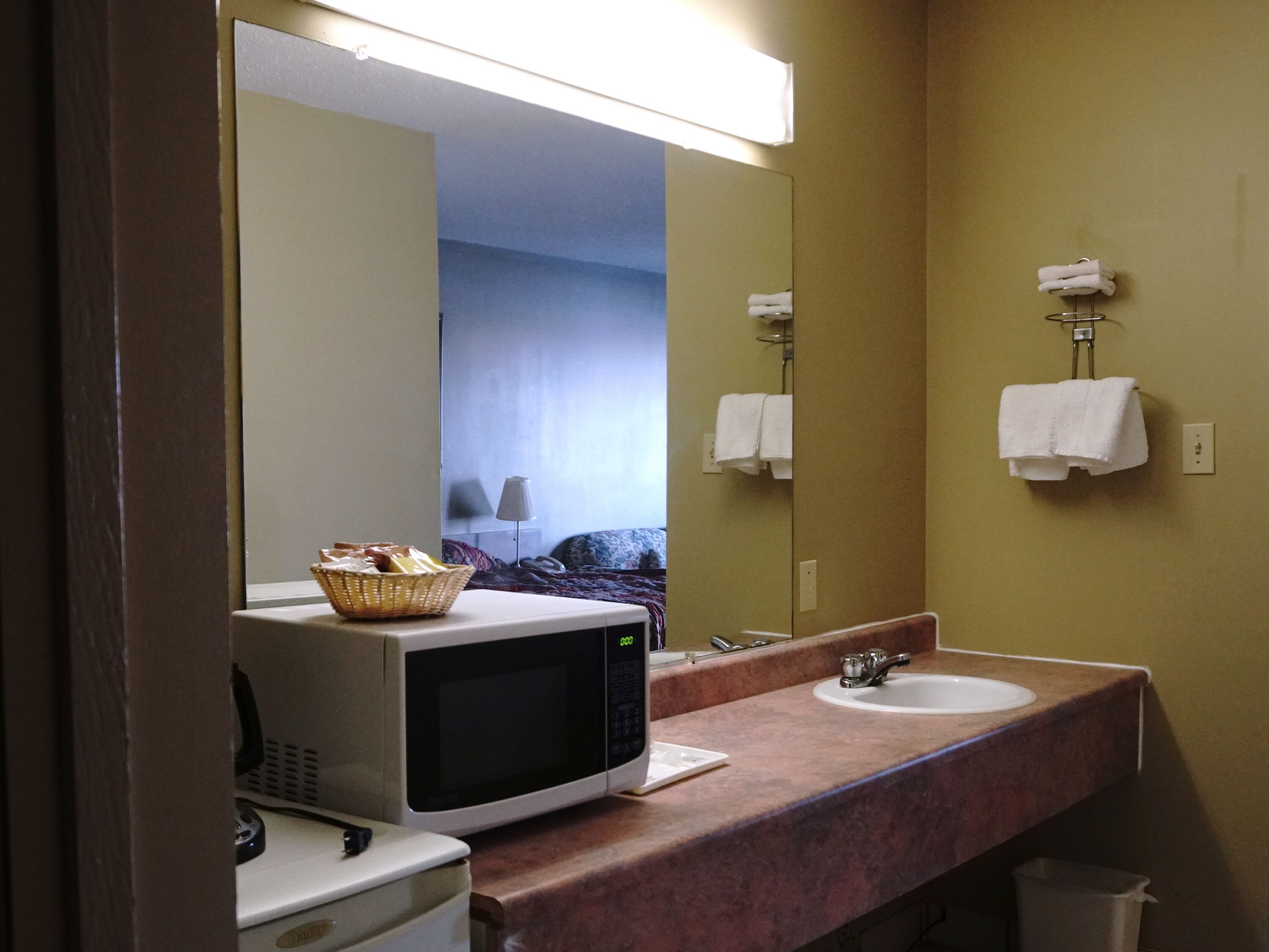 Um banheiro de hotel com um espelho grande, um micro-ondas, uma pia e uma cesta sobre o balcão.