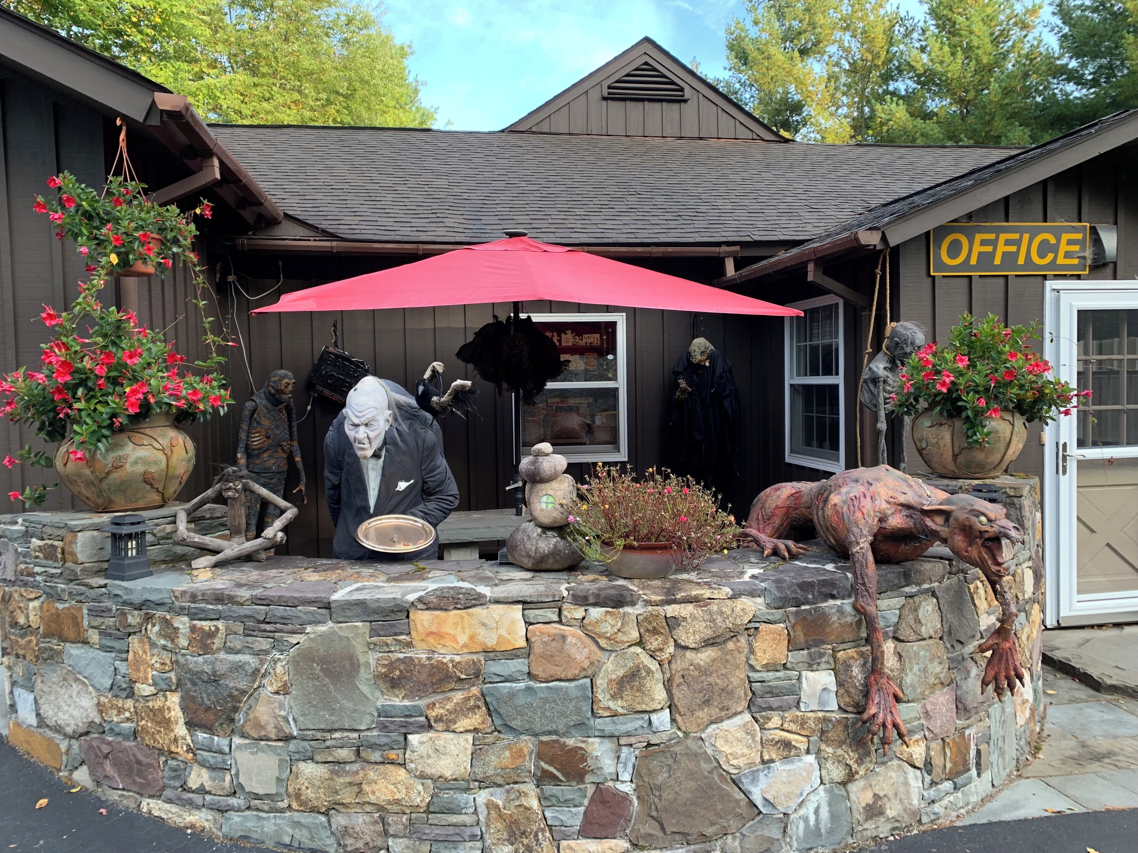 A stone wall with a rustic building, a red umbrella, and various sculptures.