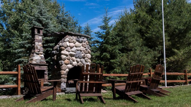 Un espacio al aire libre con una chimenea de piedra y sillas Adirondack de madera.