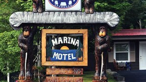 Letrero del motel Marina con el logotipo AAA Approved, estatuas de madera de osos y un muro de piedra con flores.