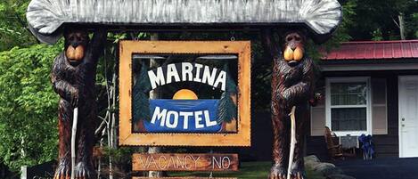 Marina Motel bord met een AAA goedgekeurd logo, houten beerbeeldjes en een stenen muur met bloemen.