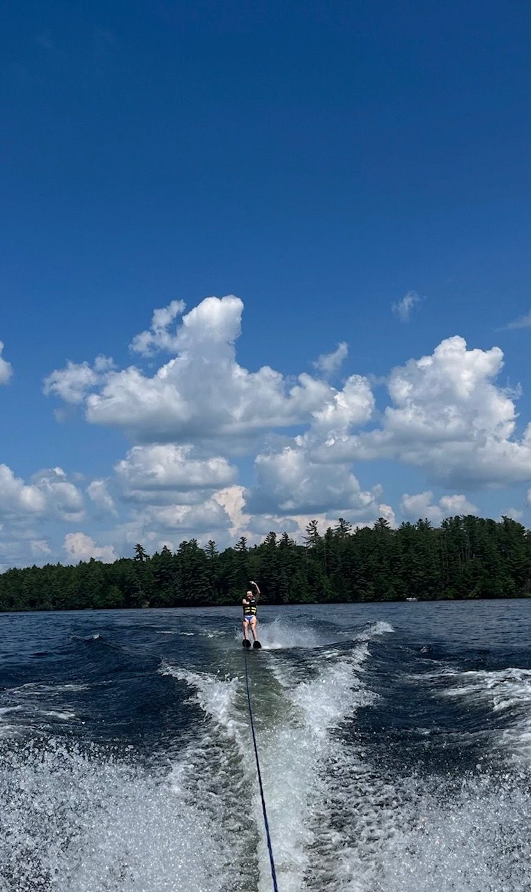 Persona fent wakeboard a un llac amb cel serè i riba boscosa.