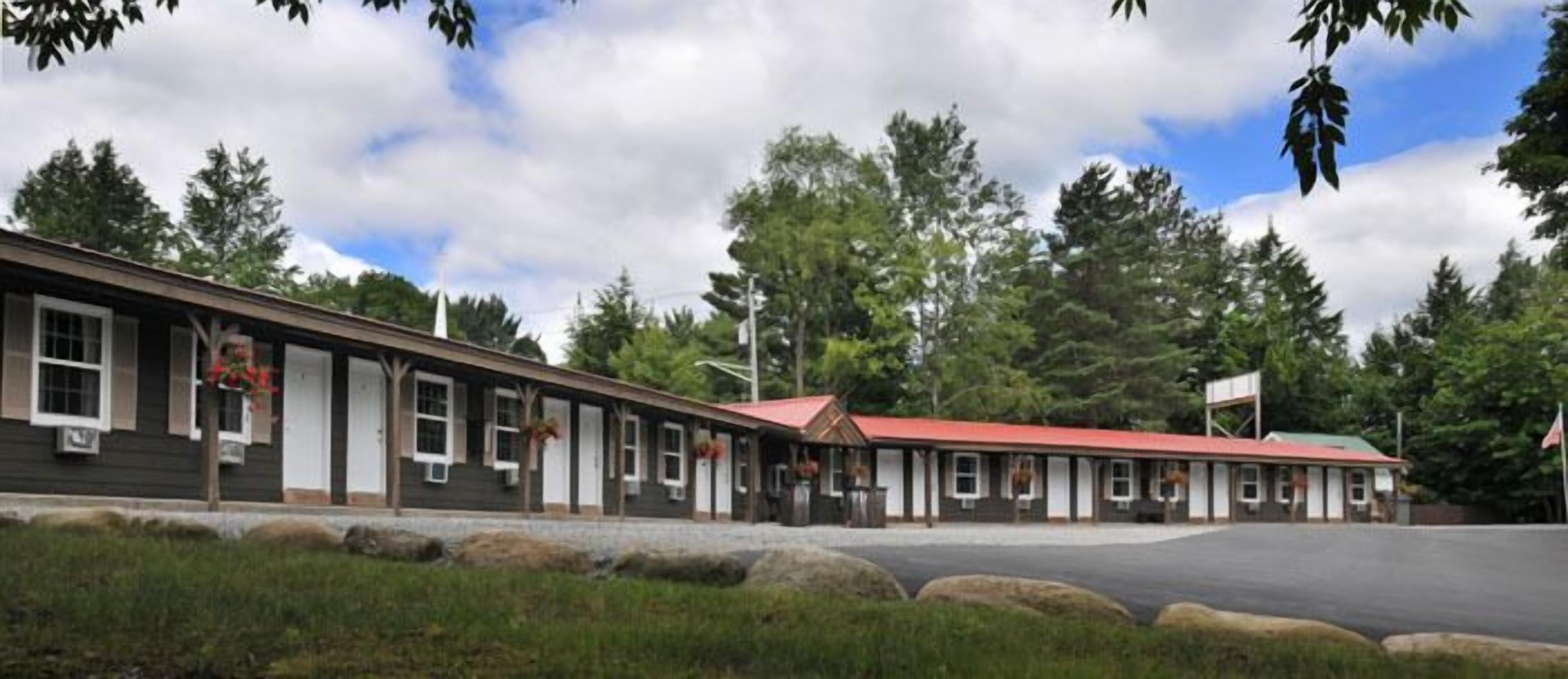 A row of single-story buildings with a red roof, likely a motel or inn, surrounded by trees and a clear sky.