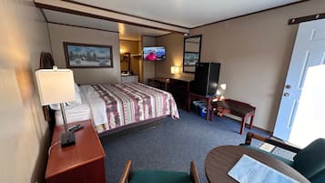 A hotel room with a bed, a desk, a chair, a television, and a door.