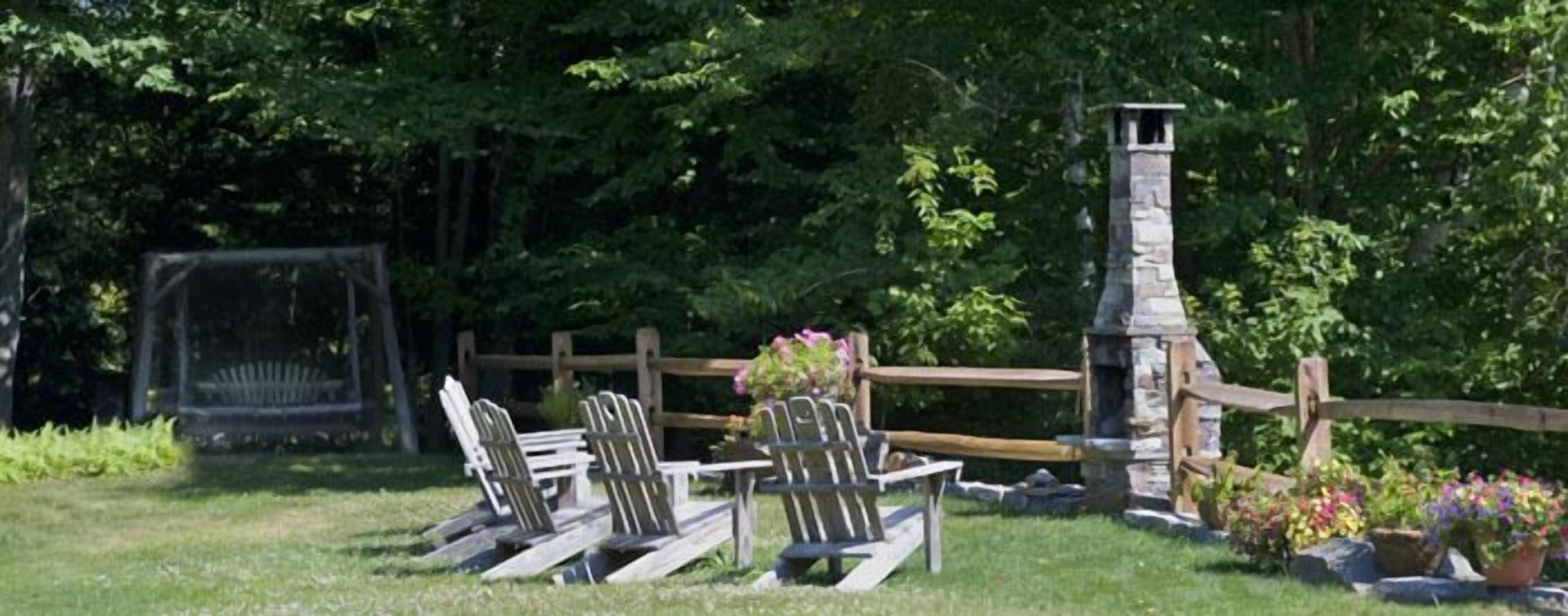 A rustic outdoor seating area with Adirondack chairs and a stone chimney.