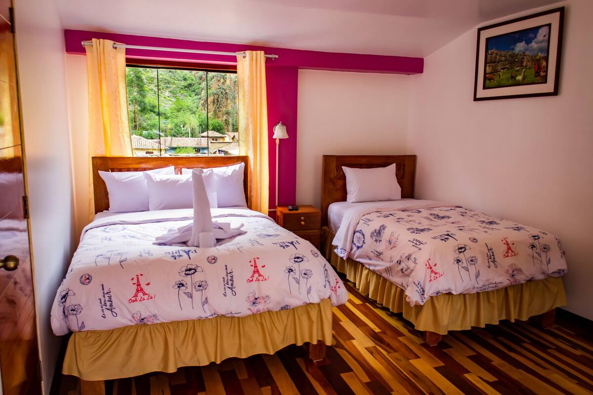 A hotel room with two beds, a window with curtains, a nightstand, and a framed picture on the wall.