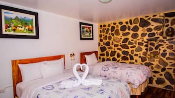 A hotel room with two beds, a stone wall, and two framed pictures on the wall.